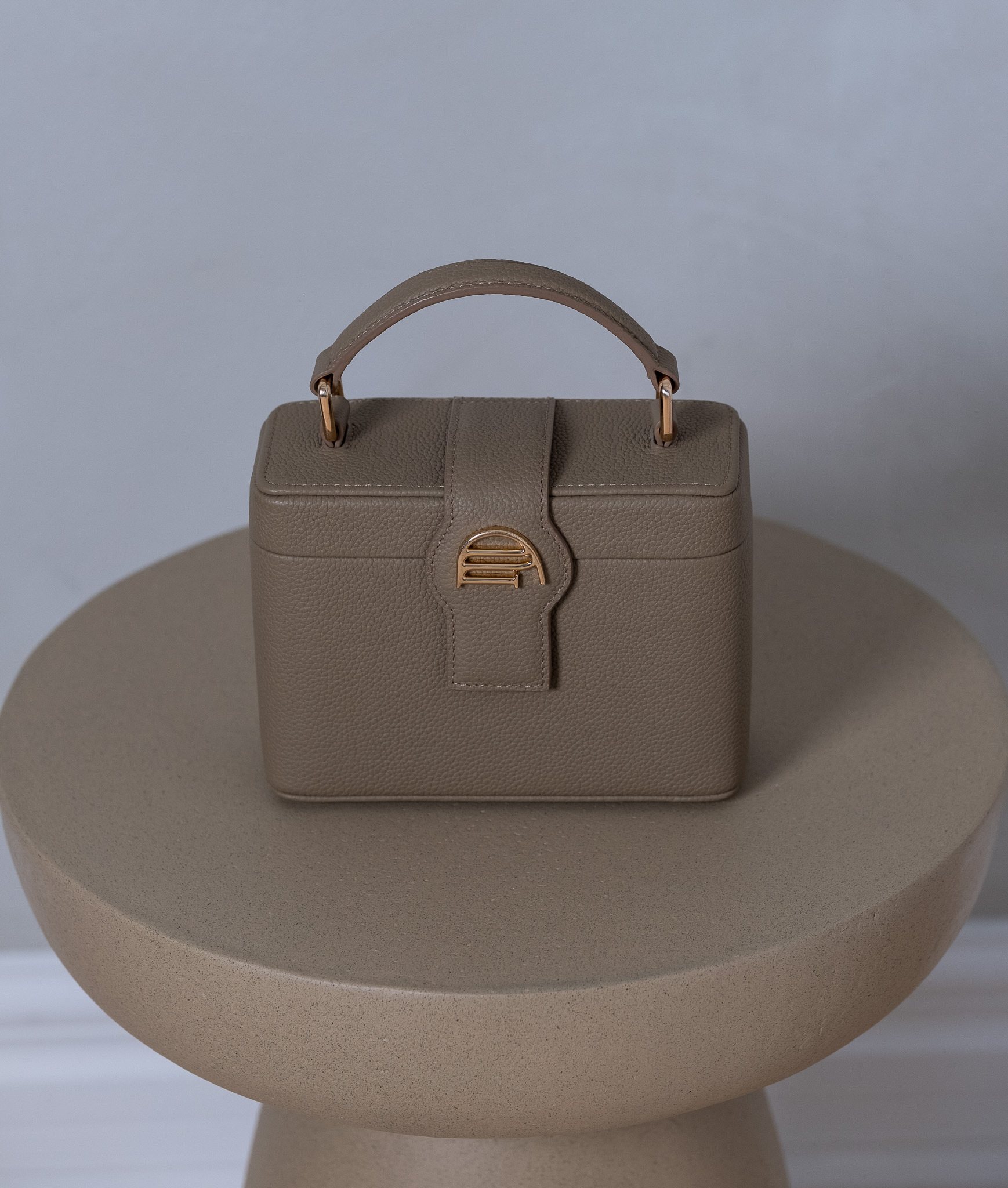 La Muse vanity bag in taupe pebbled leather with its gold-plated MOUD clasp and top handle